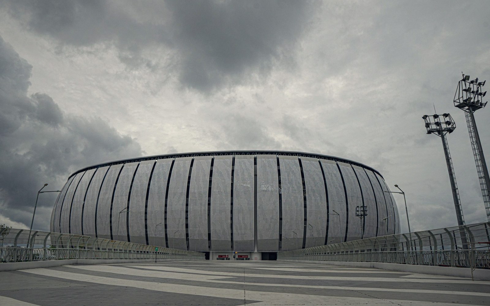 Curved stadium exterior with vertical panels under a heavy overcast sky
