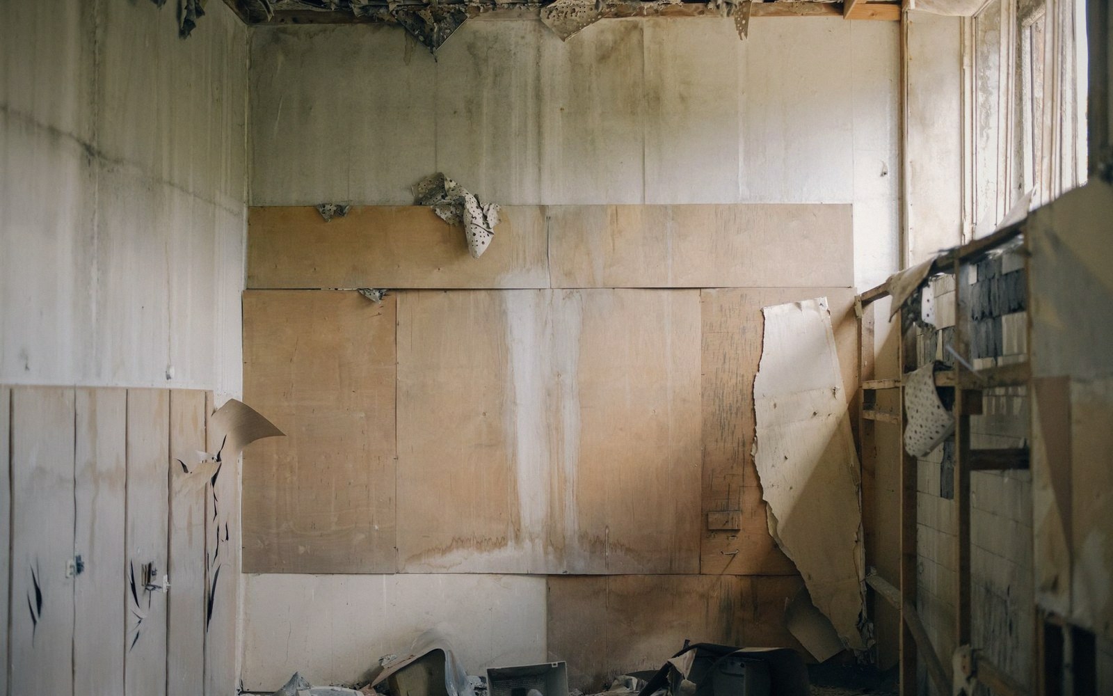 Peeling wallpaper and water-damaged walls in an abandoned room with cluttered debris on the floor
