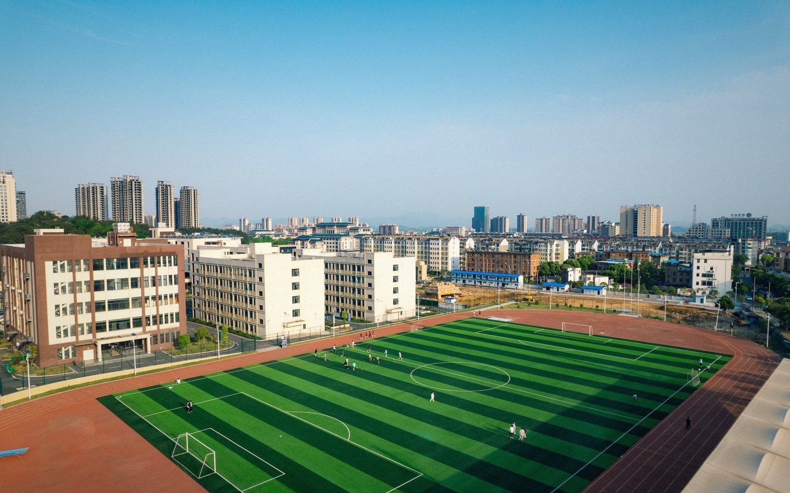 Aerial view of a school football pitch surrounded by dormitory buildings and a city skyline