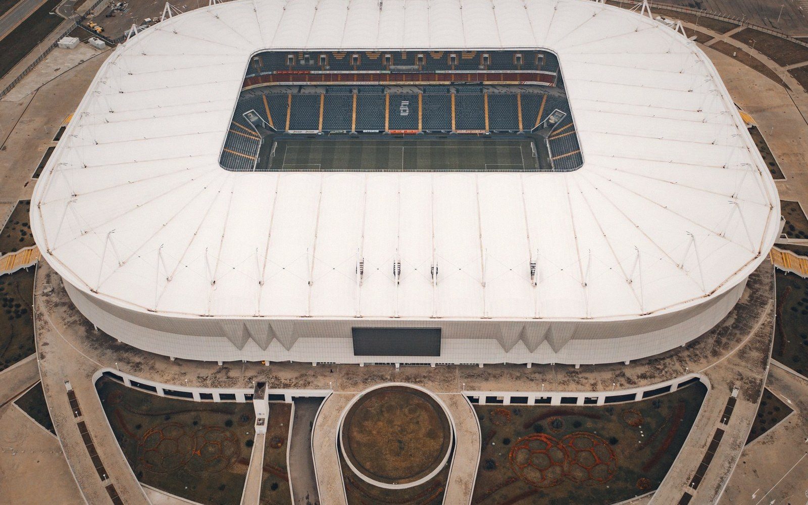 Aerial view of a stadium with a white retractable roof partially open over the pitch