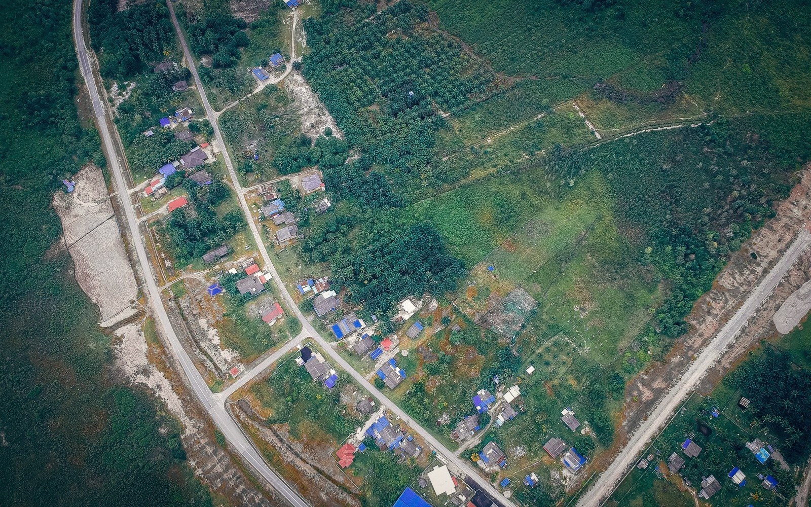Aerial view of a rural village with scattered rooftops, roads, and surrounding forested farmland