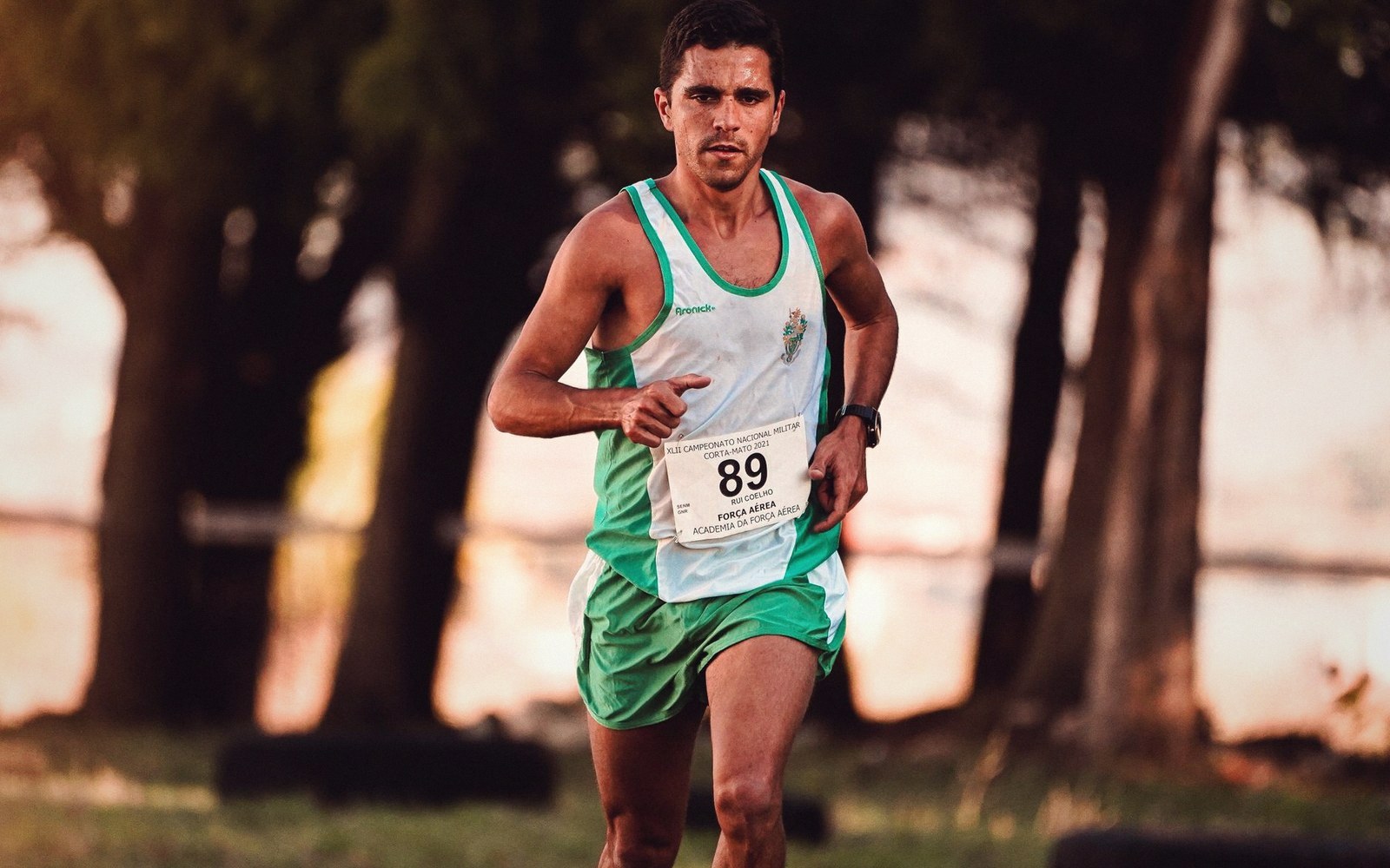 A runner wearing bib number 89 races along a tree-lined path at dusk