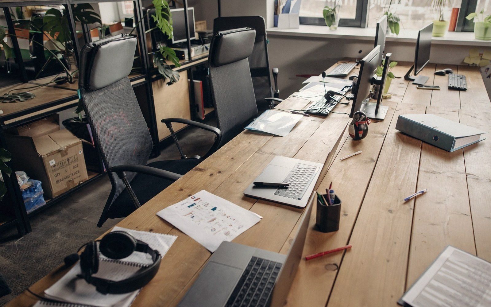 Empty office desks with laptops, monitors, and headphones left unattended on a wooden table