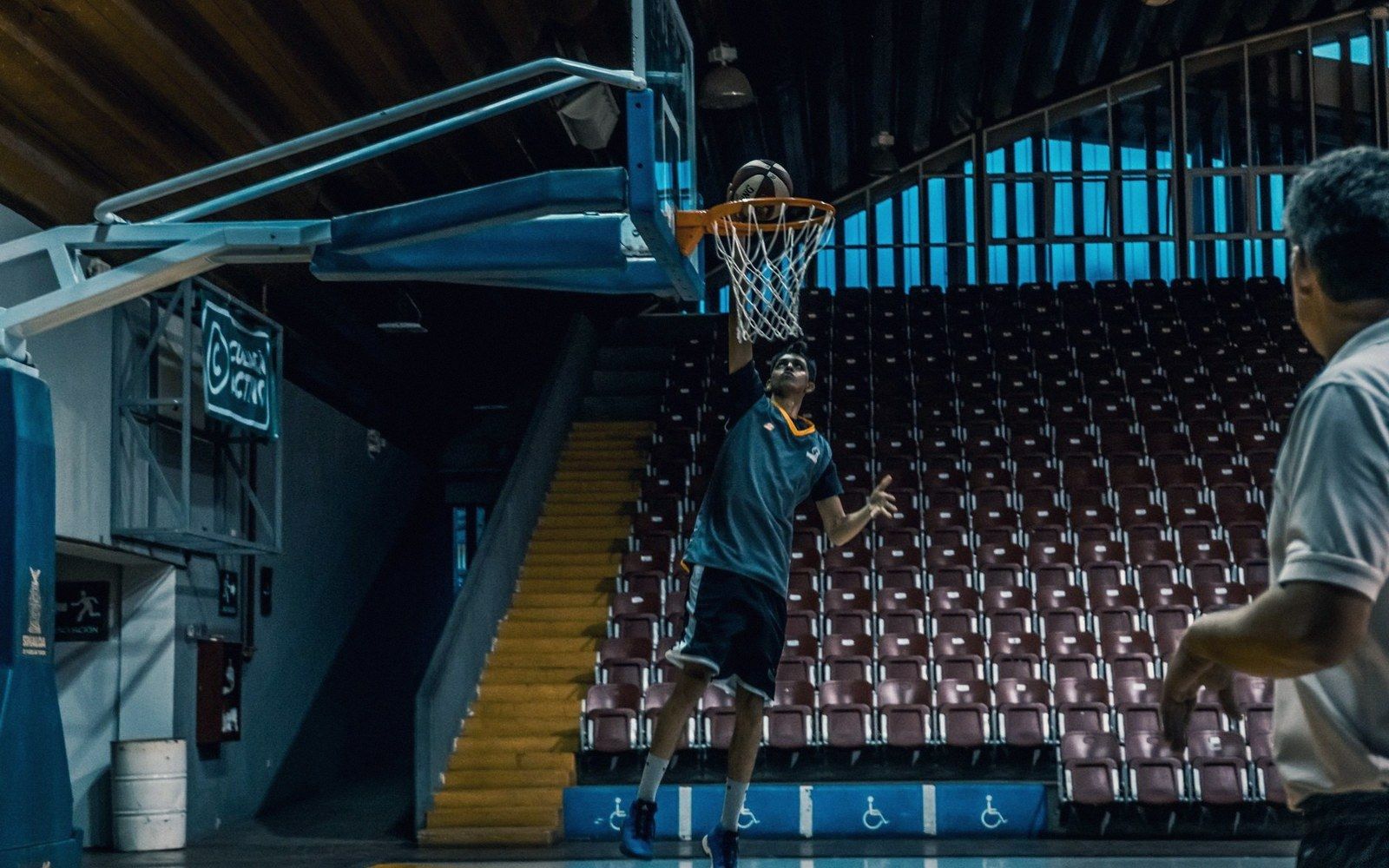 A basketball player shoots a layup near the hoop in an empty gymnasium