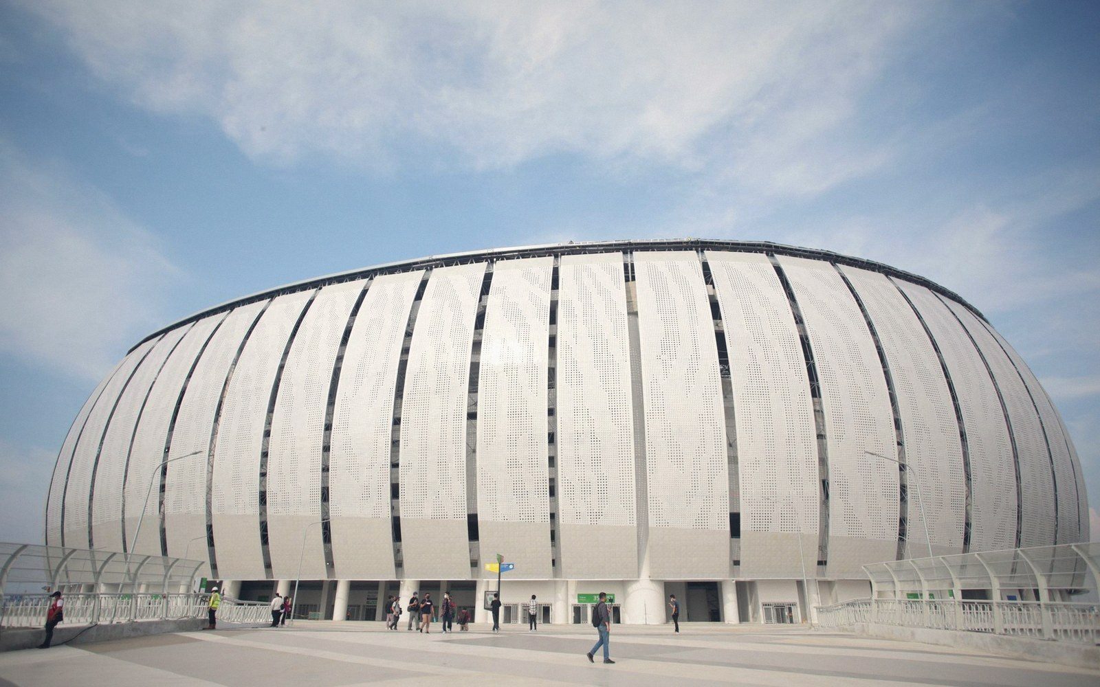 Curved oval stadium exterior with vertical ribbed panels under a blue sky