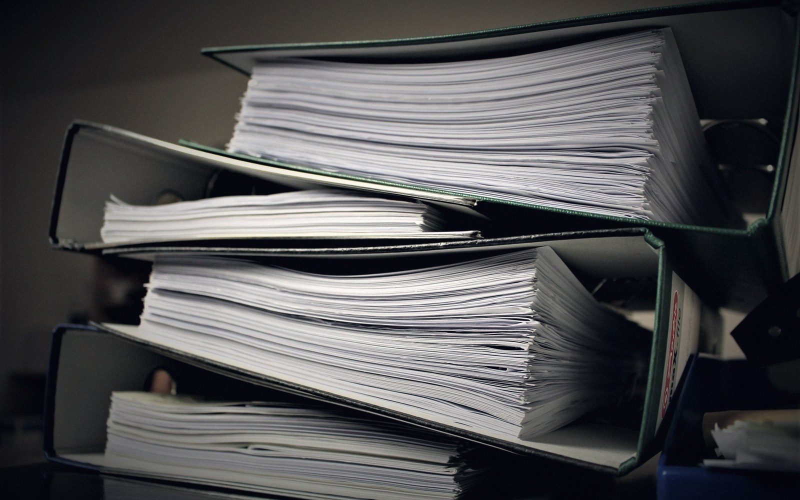 Stacked ring binders packed with paper, viewed edge-on in dim light
